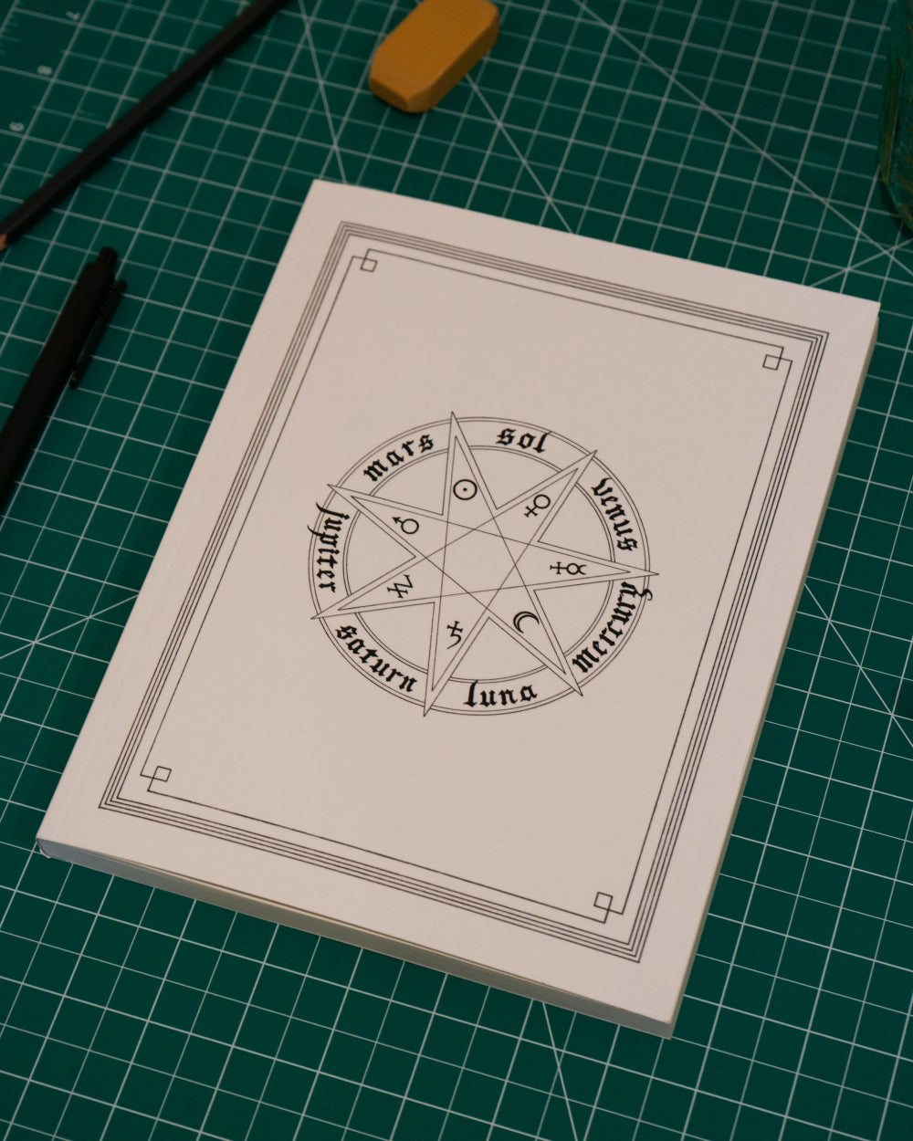White notebook with astrological symbols on a green grid surface